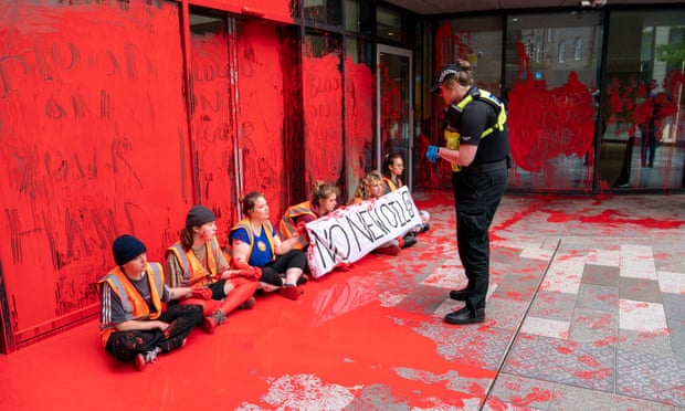 Environmental campaigners from Just Stop Oil sitting in middle of red paint with police officer talking to them