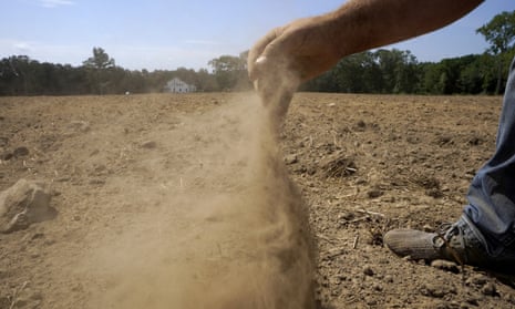 Parched field with partially seen man releasing a handful of dust
