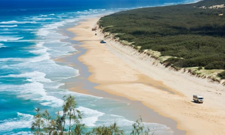 Vehicles driving down a windswept beach, seen from above