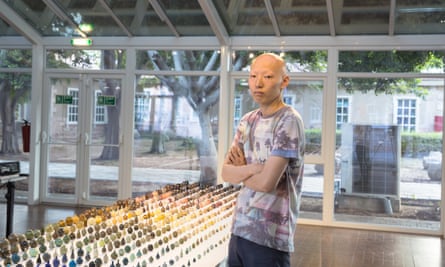 Yuta Segawa standing alongside a table covered with hundreds of his minature pots in rows.