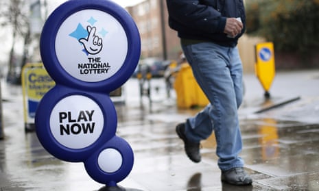 A man walks past a national lottery sign on a rain-slicked pavement