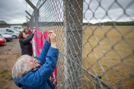 A woman attaches a bright pink banner to a fence.