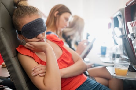 A young woman sleep on a flight in economy class with an eye mask on.