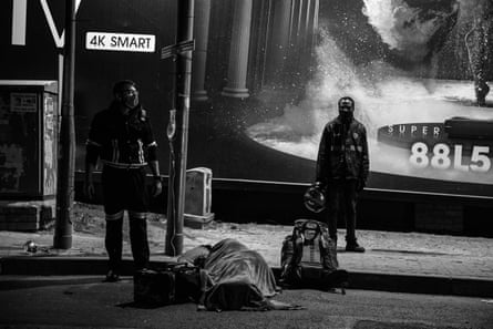 A seriously injured food courier waits for an ambulance together with a paramedic, as nother driver watches the scene