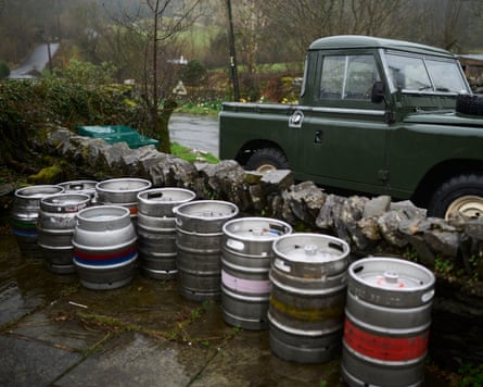 A line of beer kegs in a driveway. A green car is in the background.