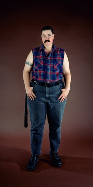 Catherine Opie dressed in drag as someone with a moustache with short hair and wearing a flannel vest, blue jeans and black boots