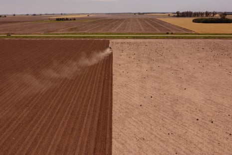 A tractor raising dust in a vast field which is half ploughed and half not, in an endless landscape in Argentina