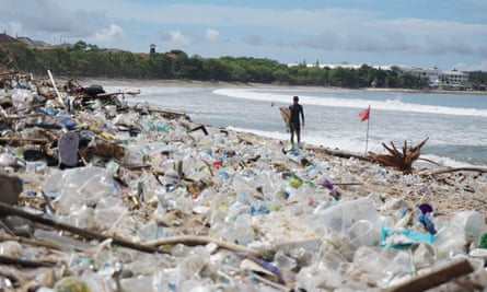 A surfer stands before mounds of garbage on Bali’s famous Kuta Beach