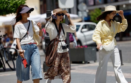 Three women walking along a pavement wearing wide-brimmed hats