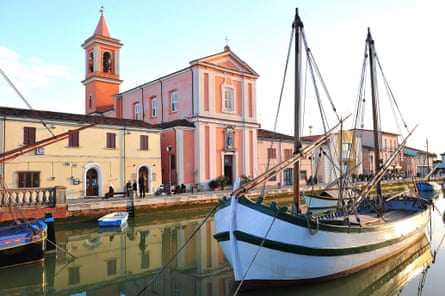 A boat in front a pink church in the port of Cesenatico (Italy)
