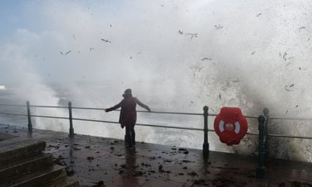 A woman braces herself as waves crash against the sea wall in Penzance, Cornwall
