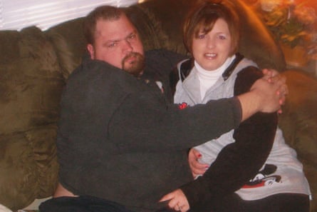 A man wearing a black top with his arms round a woman wearing a grey and white top looking at the camera