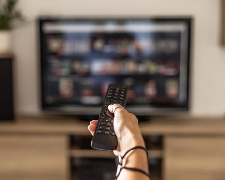 A close-up of a hand pointing a remote control towards a blurred television screen