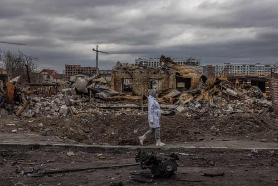 A woman walks past destroyed houses on the street in Bucha.