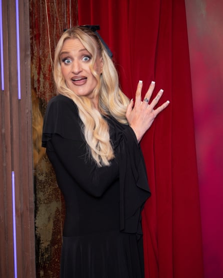Daisy May Cooper peeks out from behind a red curtain with a surprised expression