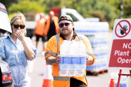 A man in orange hi-vis delivers bottles of ‘courtesy water’ in a Whitstable car park