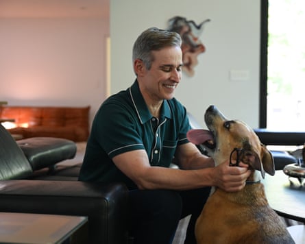 Sitting on a leather chair, he smiles as he strokes the dog in front of him