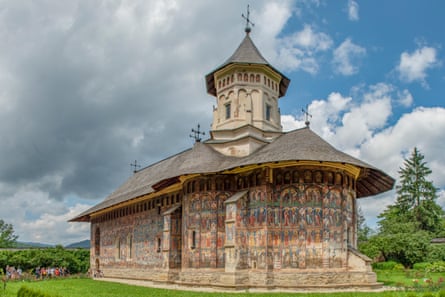 A church with a pointed tower and frescoes all over the outside