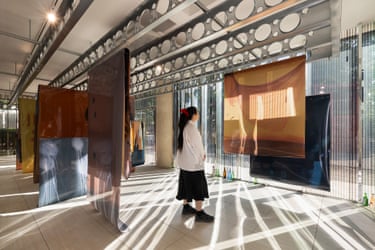 A woman views large hanging fabric panels in a sunlit art installation at Bvlgari Pavilion