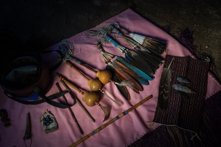 An array of tools made of feathers, beads and perhaps small gourds in a line on a thin pink shawl.