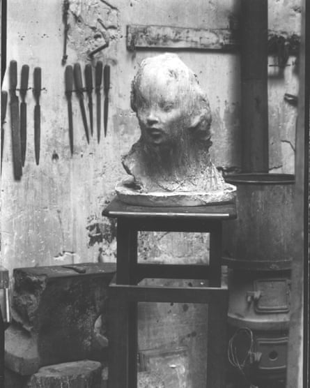A black-and-white photo of a sculpture of a human head resting on a stool in a workshop