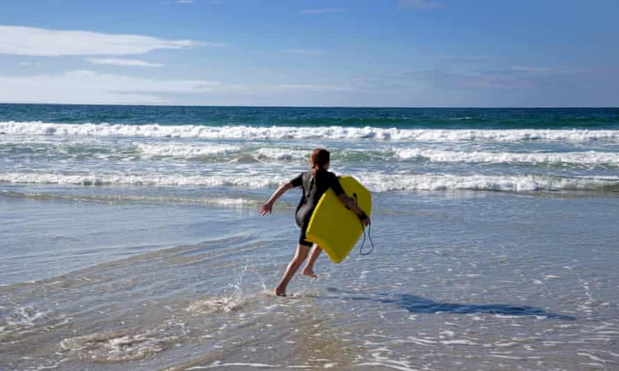 Joven vistiendo traje de neopreno corriendo hacia el mar con tabla de surf