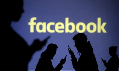 Mobile phone users stand near a Facebook logo.