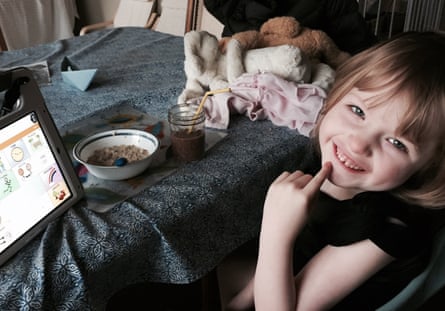 a child smiles while sitting at a table with food a drink and a tablet