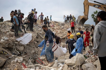 Volunteers remove a body from wreckage while others watch