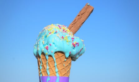 A blue ice-cream with a chocolate flake in it, in a cone, against a blue sky