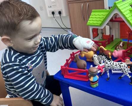 Boy playing with a farm animal set while receiving a transfusion