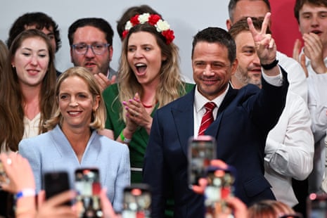 Rafał Trzaskowski holding up his hand in a V for victory sign beside his wife and surrounded by supporters