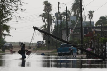 A man carries items through floodwater past downed electric lines