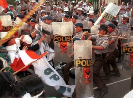 Uniformed officers with riot shields and long sticks clash with protesters waving red and white flags