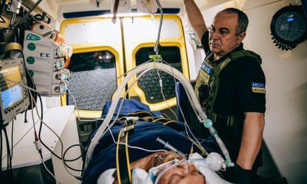 A Ukrainian medic looks at equipment readings as he stands next to an intubated patient on a makeshift bed in the back of a van