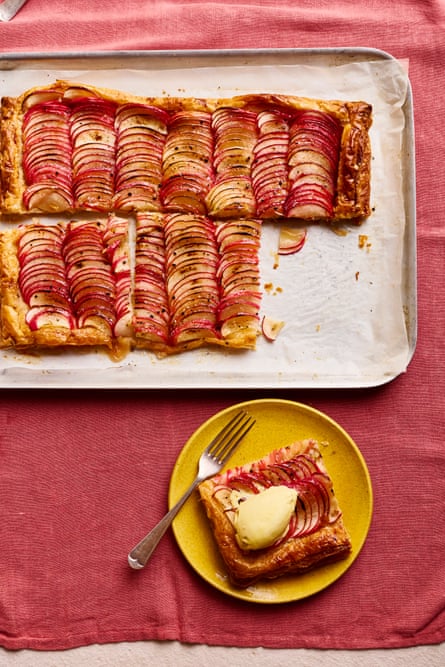A tray of apple puff tart on a red cloth, alongside one serving on a plate with a fork and a dollop of ice cream.