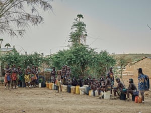 A group of women wait with plastic tubs for water
