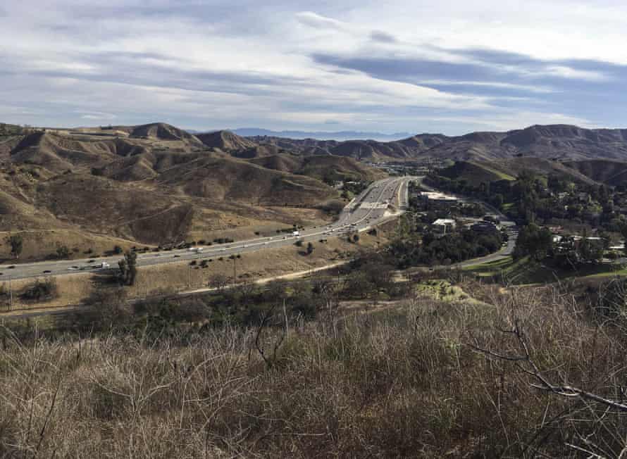 An eight-lane wide highway cuts through a mountainous landscape with wilderness on either side.