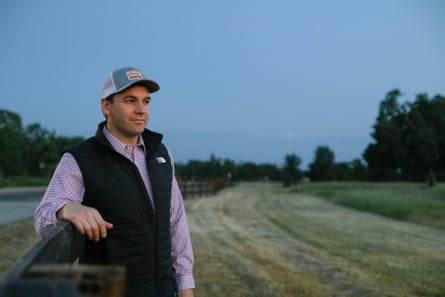 man wearing hat, black vest and checkered button-down in a field