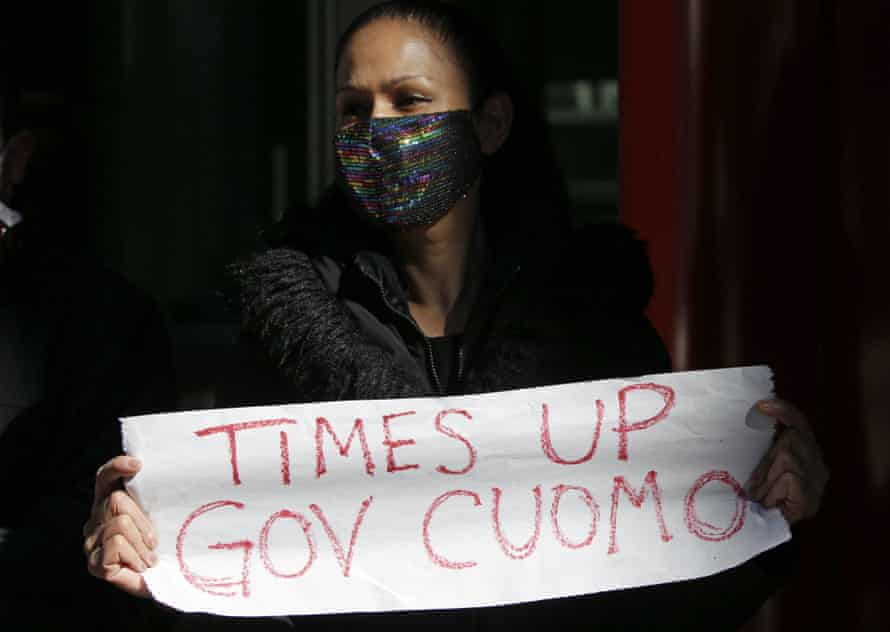 A woman attends a protest holding a sign that reads 'Time's up Gov Cuomo'.