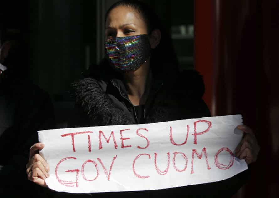 A woman attends a protest holding a sign that reads “Time’s up Gov Cuomo”.