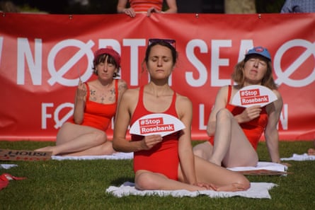 Three women in red swimsuits hold up signs saying Stop Rosebank on grass