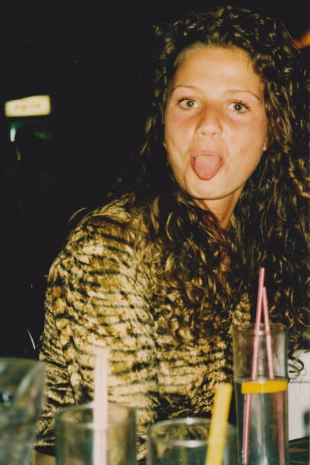A woman with dark brown curly hair in a tiger-skin jacket poking her tongue out