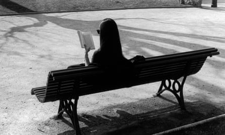 Woman sat alone on bench reading a book.