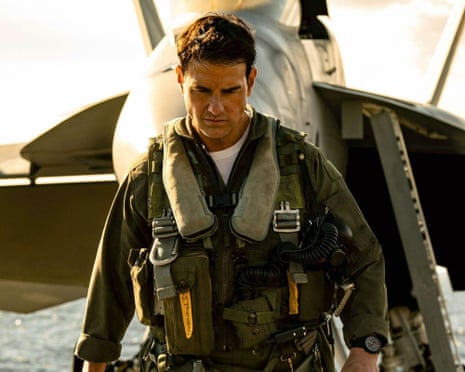 man in navy pilot uniform stands in front of plane and looks down