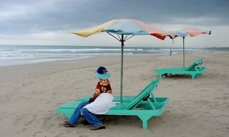 A woman sits on an empty beach chair in Kuta beach, Bali, Indonesia