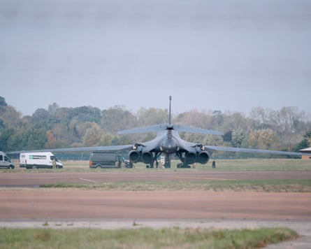A US Air Force Rockwell B-1 Lancer bomber on tarmac at airfield with ground support vehicles gathered around.
