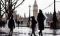A family walks along the Southbank in the rain with The Palace of Westminster, home to the Houses of Parliament, in the background, in London