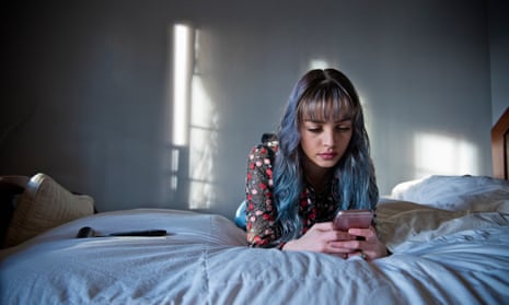 Teenage girl lays on her bed looking at her phone