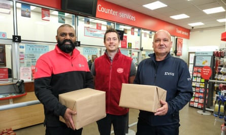 Three workers, two of tyhem hoplding parcels, in a post office; each wearing company flleces - one from DPD, one from Royal Mail and one from Evri